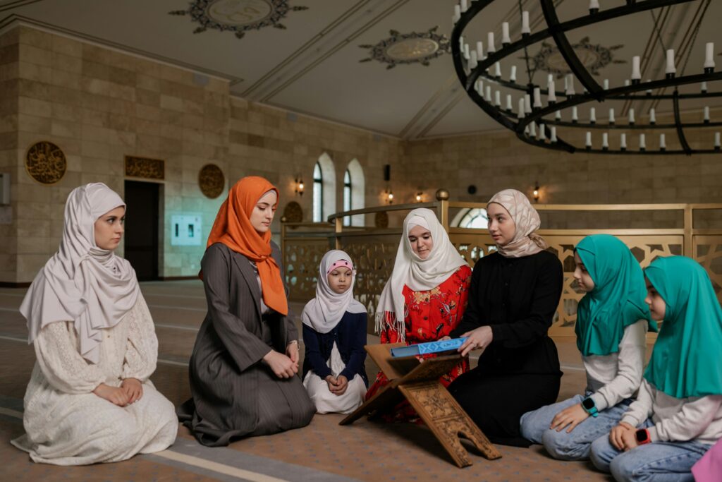 Women and children wearing headscarves praying inside a mosque for religious gathering.